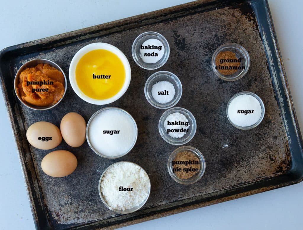 ingredients for pumpkin bread on a baking sheet on a white countertop