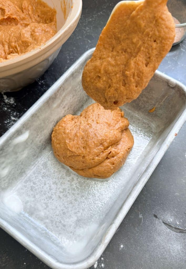 spooning pumpkin bread batter into greased loaf pan 