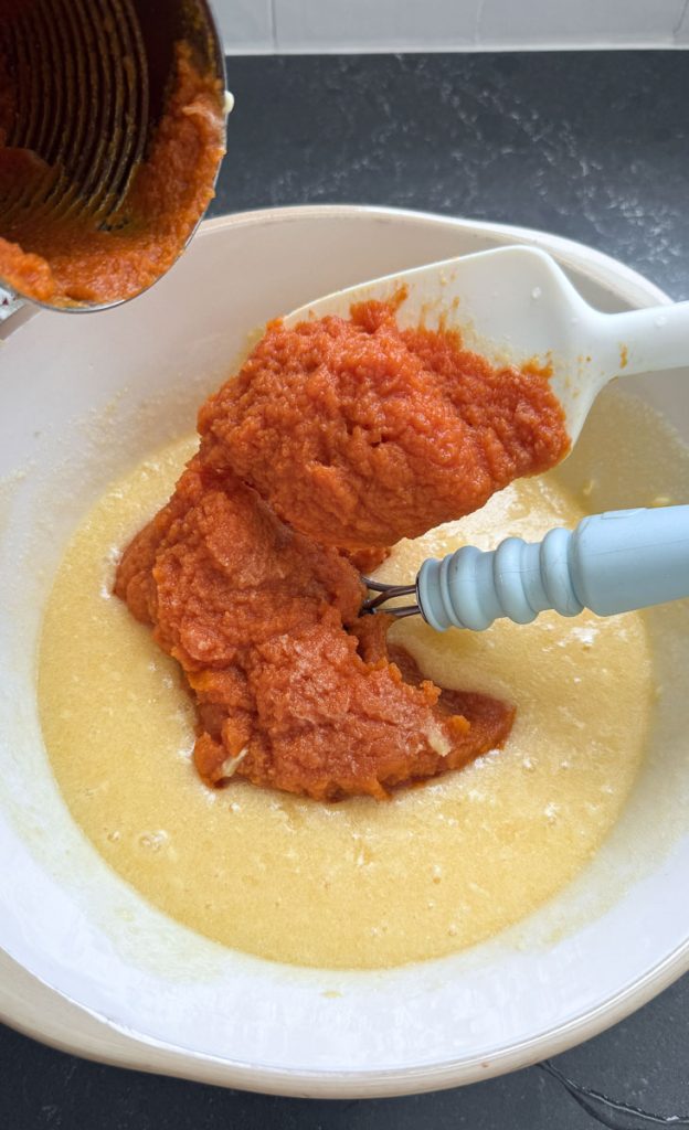 adding pumpkin to butter sugar mixture with a white spatula 
