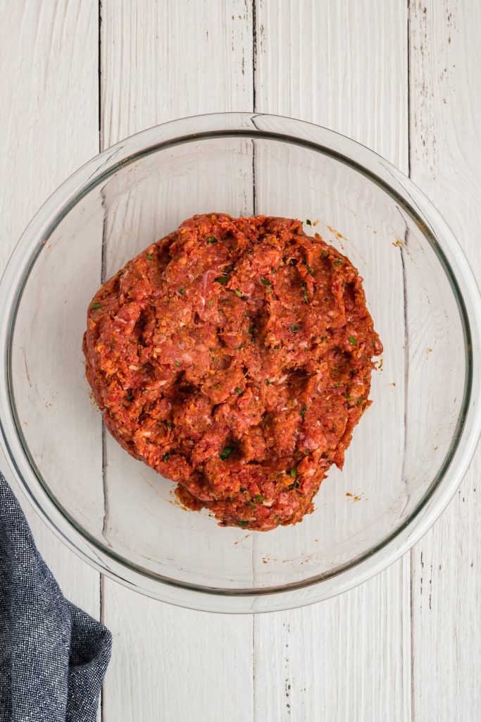 glass bowl on a white surface with raw ground beef meatloaf mixture in the bowl