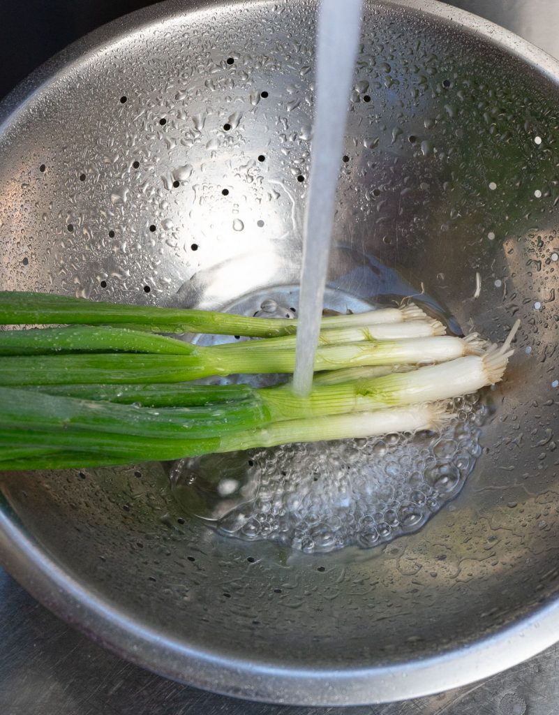 washing green onions in a metal colander 