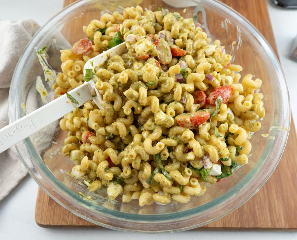 mixing bowl of pesto caprese pasta salad with a large white spatula