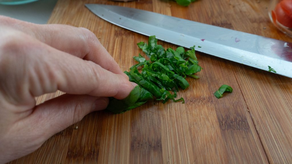 Chiffonaded basil on a wood cutting board with the knife in the background
