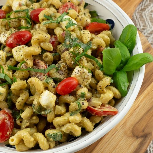 noodles, tomatoes, basil, mozzarella pasta salad in a white bowl on a wood cutting board