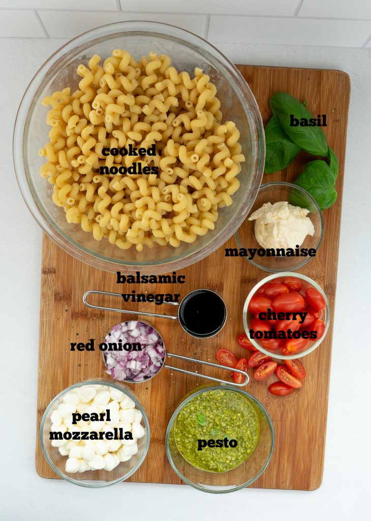 ingredients for pesto caprese pasta salad layed out on a wood cutting board on a grey counter top