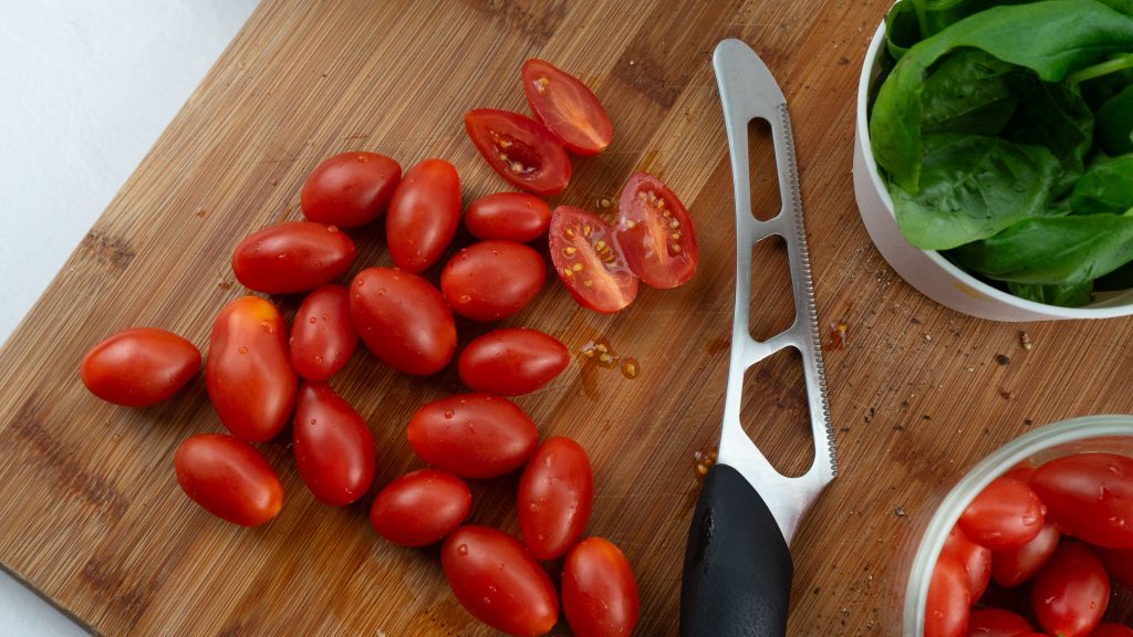 cherry tomatoes on a cutting board with a knife, cherry tomatoes cut in half, bowl of basil