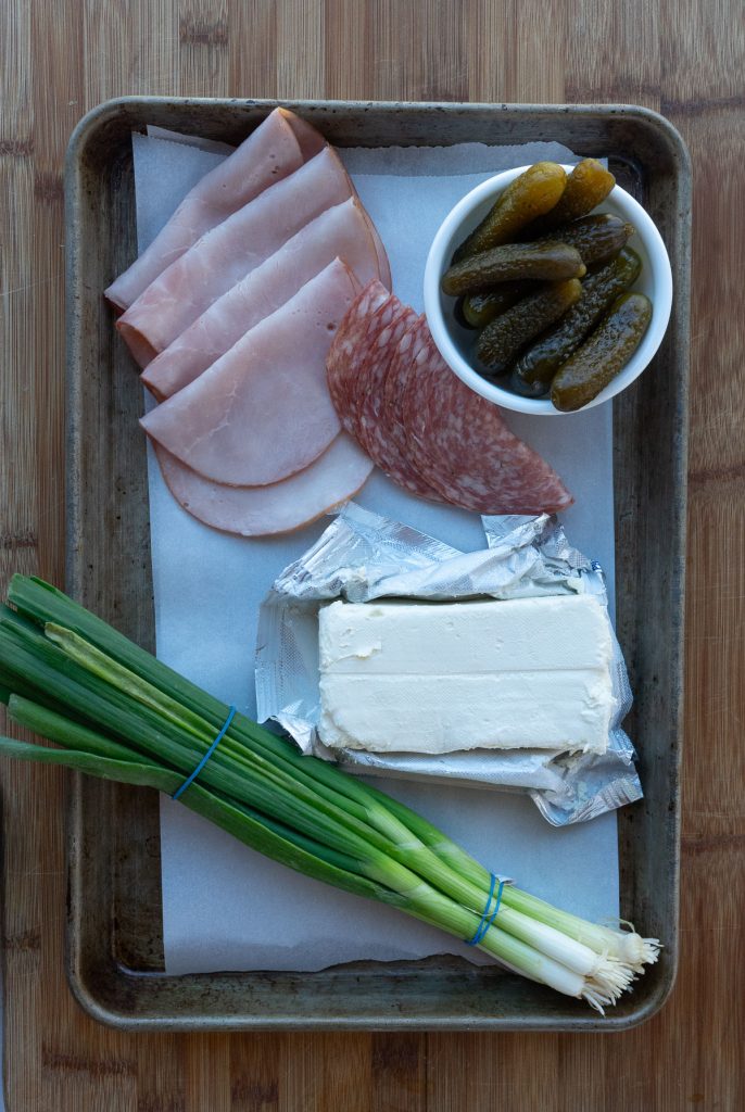 sheet pan with ingredients: ham, salami, gherkins, cream cheese, green onions 