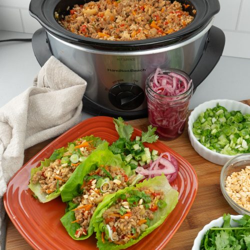 chicken lettuce wraps with slow cooker full of meat in background accompaniments on the side