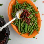 Green beans, on a orange platter with sweet and sour bacon sauce being spooned over green beans