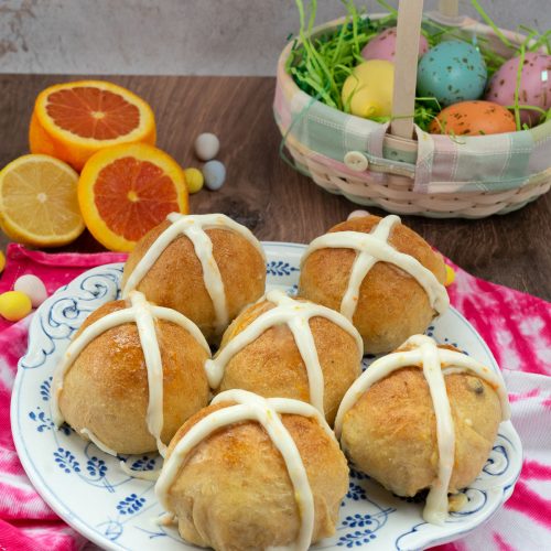 hot cross buns on a plate with easter decorations around the plate