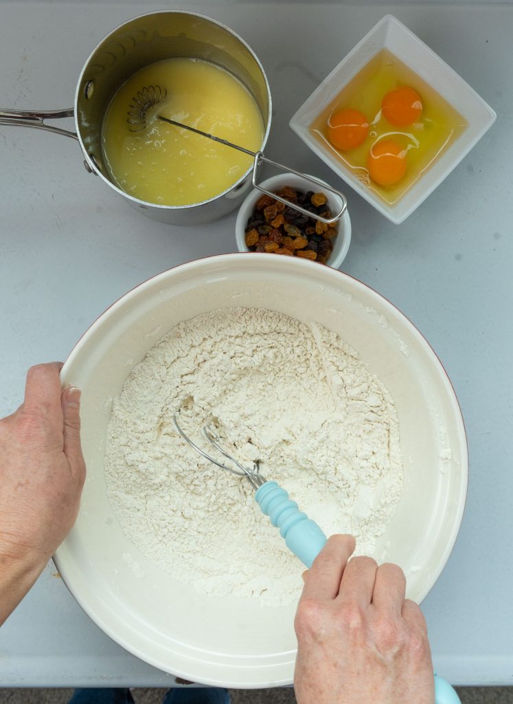 mixing ingredients. milk, butter in pan, dry ingredients in bowl, eggs in white dish, raisins in small white dish