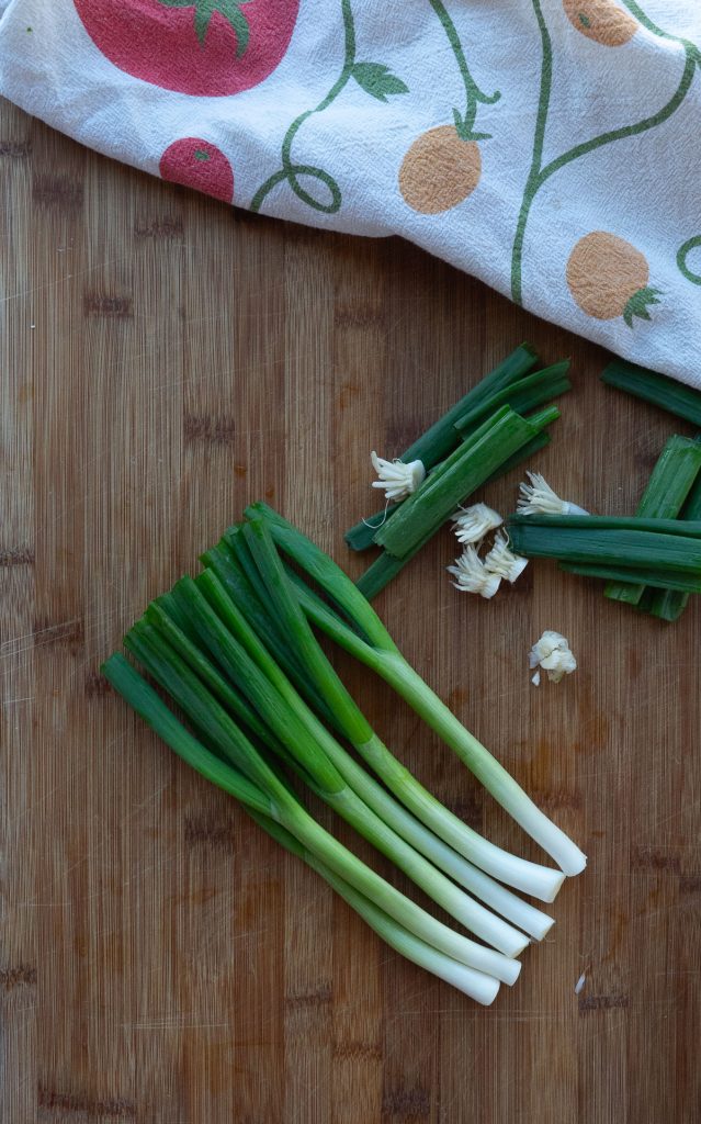 green onions on a wood cutting board with trimmed tops and ends off to the side