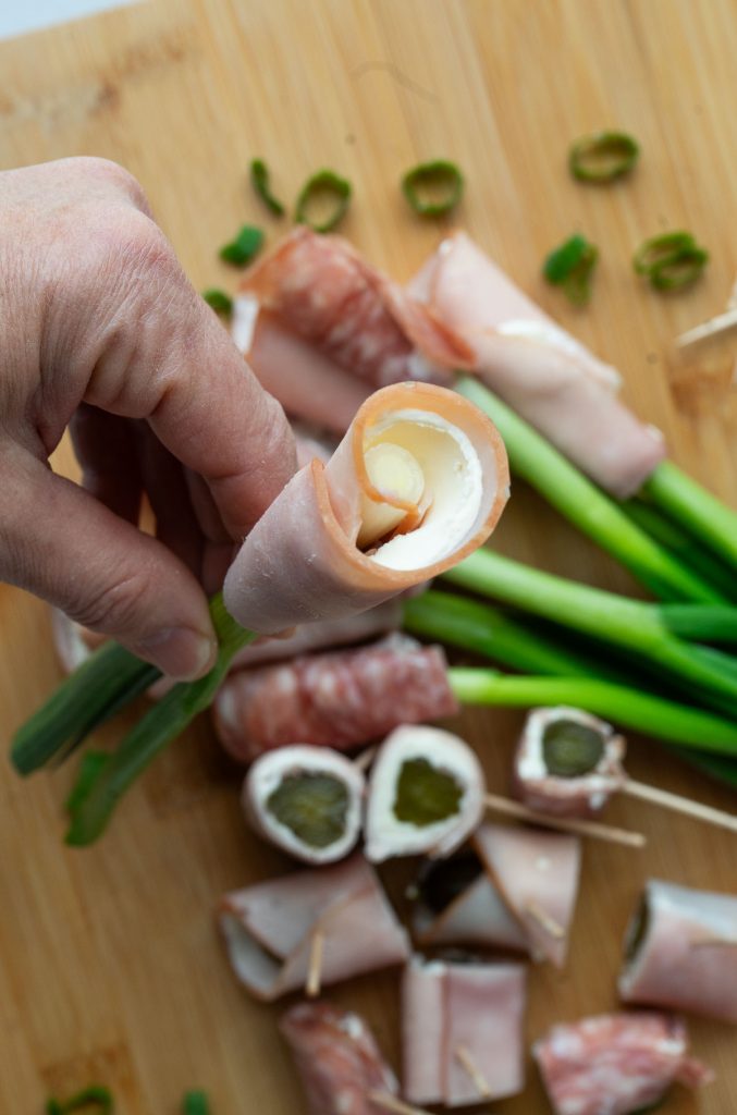 hand holding a ham wrapped green onion with appetizer board in background