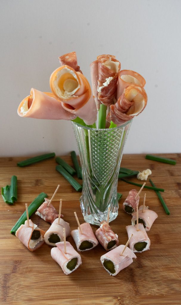 ham rolls ups in a vase surround by pickle roll ups on a wood cutting board