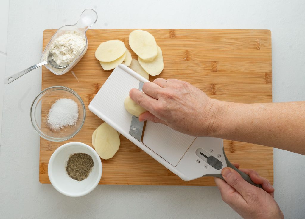 slicing peeled potatoes with a mandoline slicer