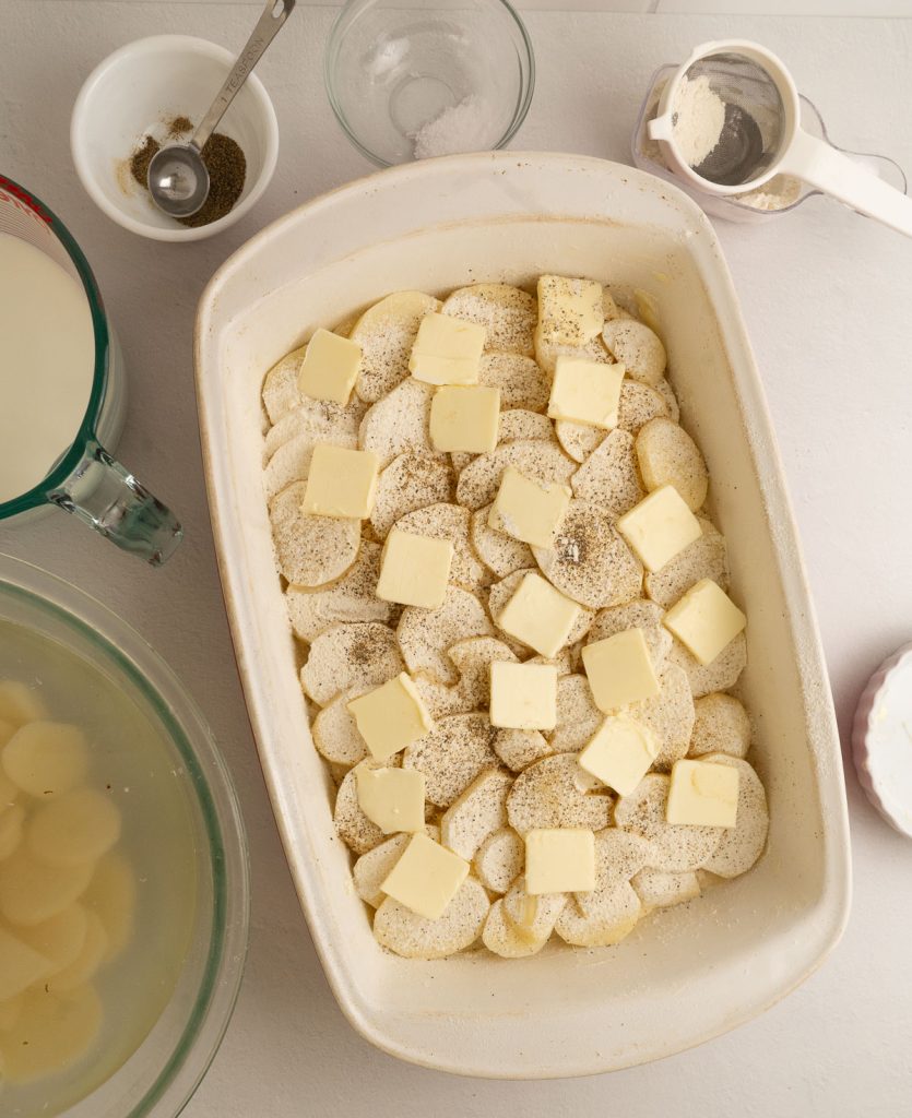 process photo of scallop potatoes raw potatoes layered in flour salt pepper and butter slices