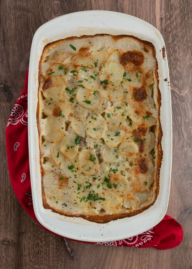 casserole dish of scallop potatoes on wood background with a red bandana towel wrapped around the side