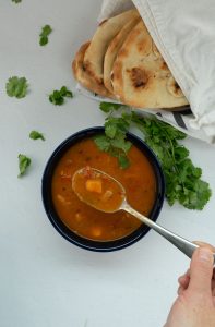 Bowl of sweet potato soup on a white background with green garnish and naan bread wrapped in a white towl off to the side