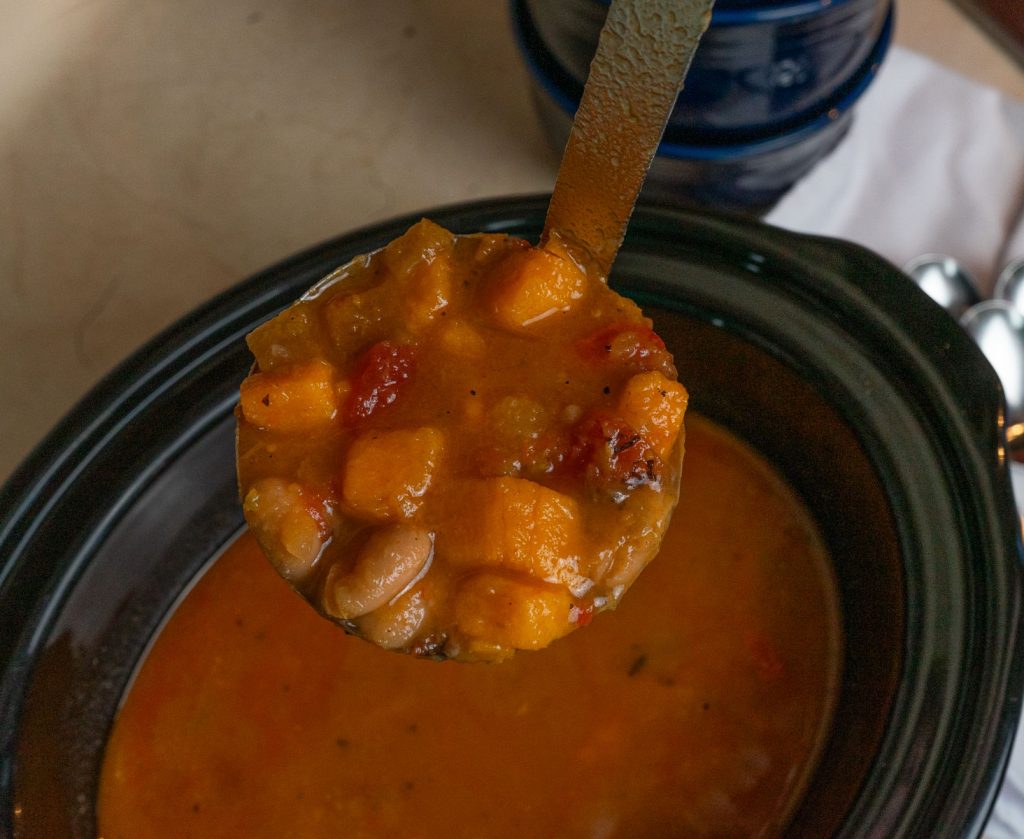 ladle of sweet potato curry soup over slow cooker full of soup