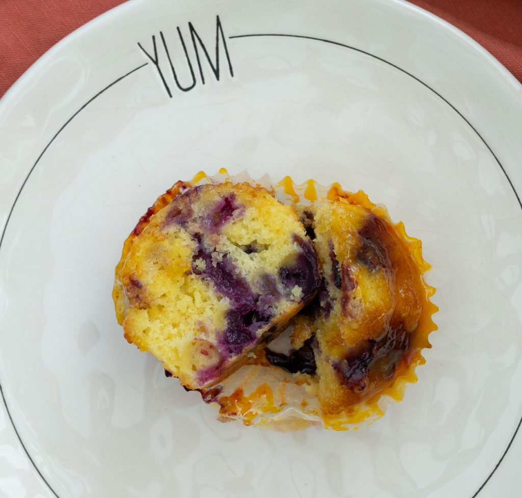 orange muffin with blueberries added to it on a white plate with the word yum at the top