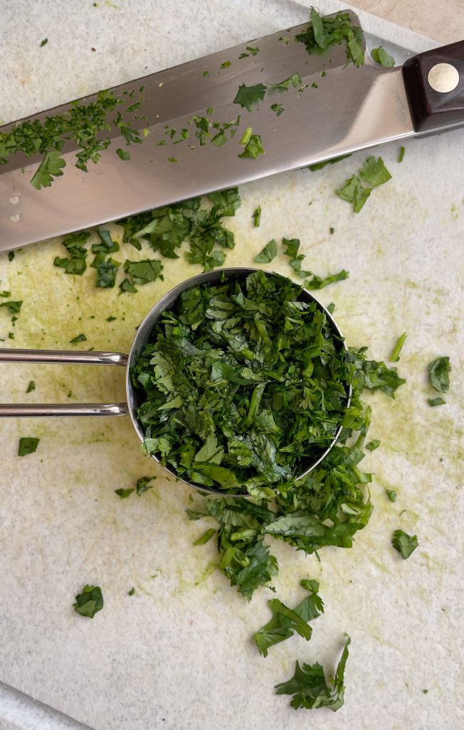chopped cilantro on a cutting board in a silver measuring cup with a knife on the board