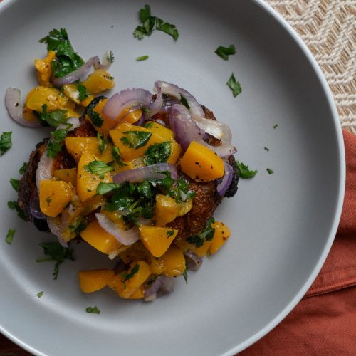 Peach cilantro salsa on top of a grilled pork chop on a gray plate