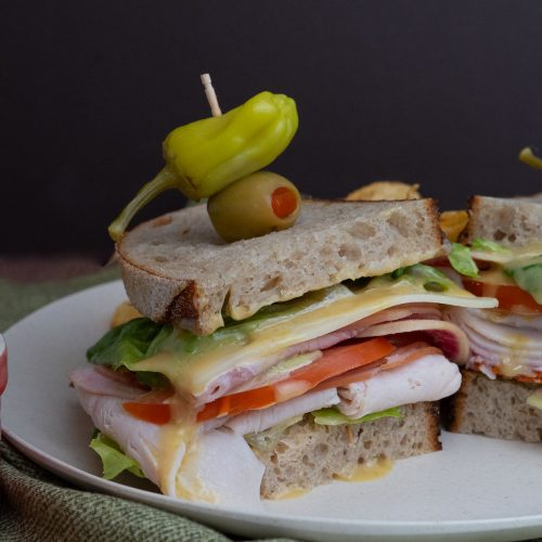 deli meat sandwich on a plate with a pickle and an olive on top with a toothpick