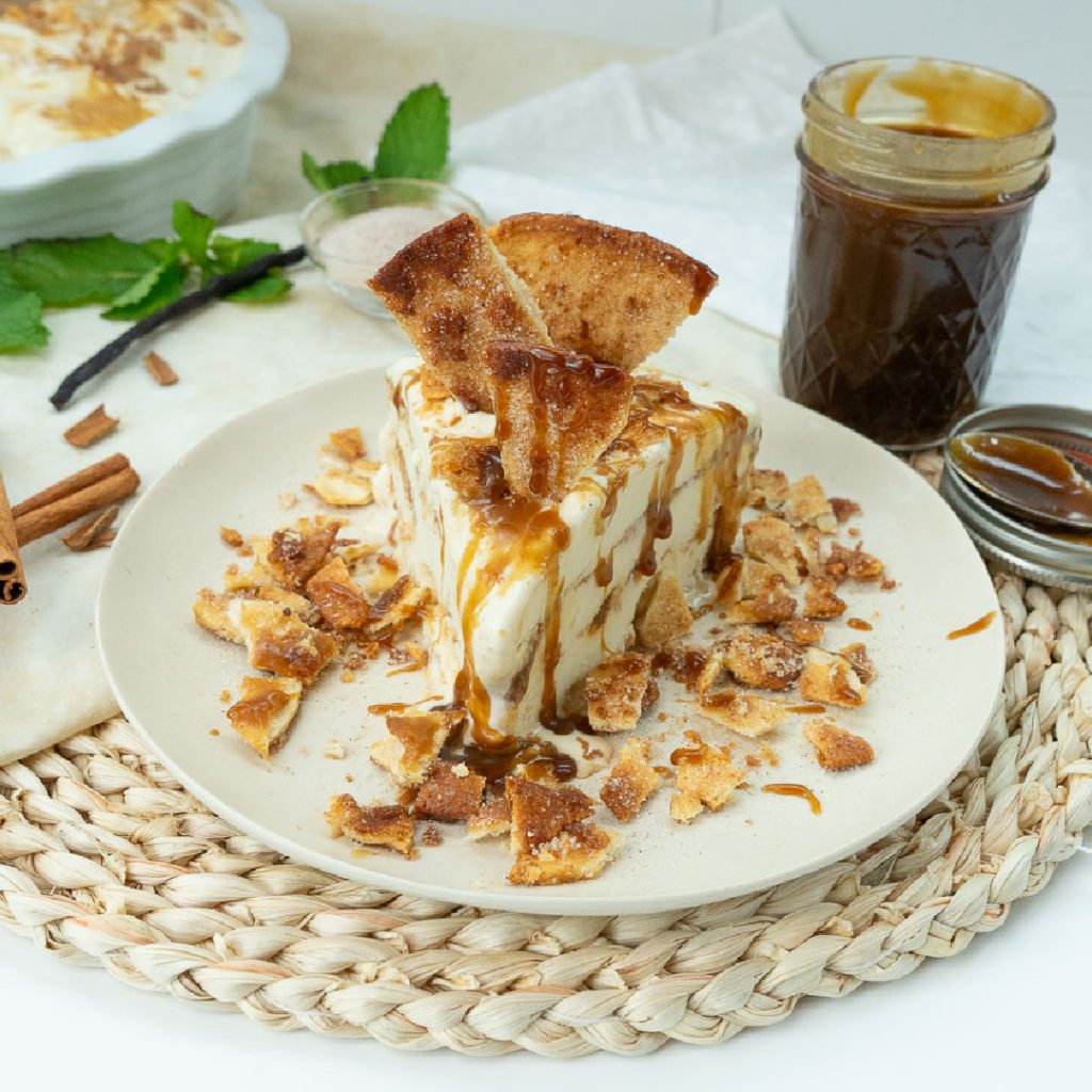 Slice of churro ice cream pie on a white plate with caramel sauce and a jar of caramel sauce in the background 