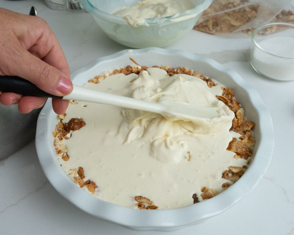layering vanilla ice cream in churro ice cream pie