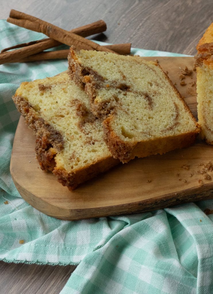 two slices of cinnamon streusel bread laying on a wood board with a mint and white checked cloth under the board