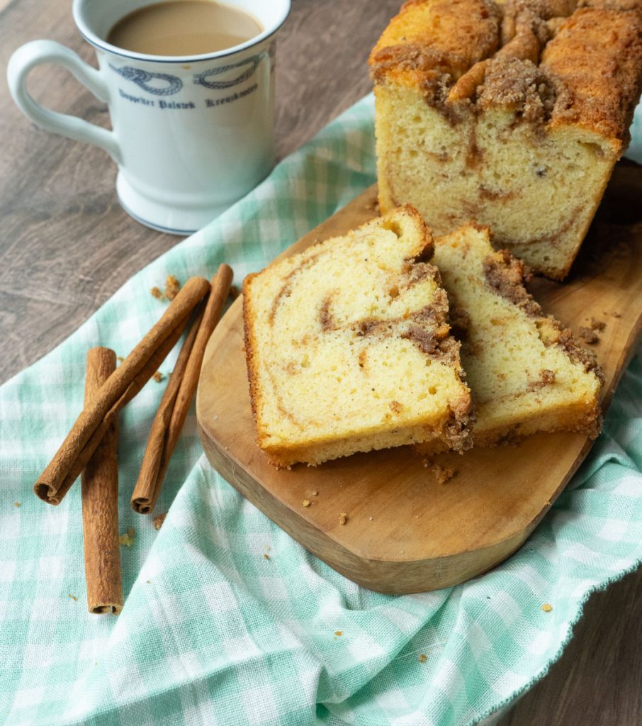 photo of cinnamon bread on a wood plank with 2 slices cut from loaf, cup of coffee off to the side
