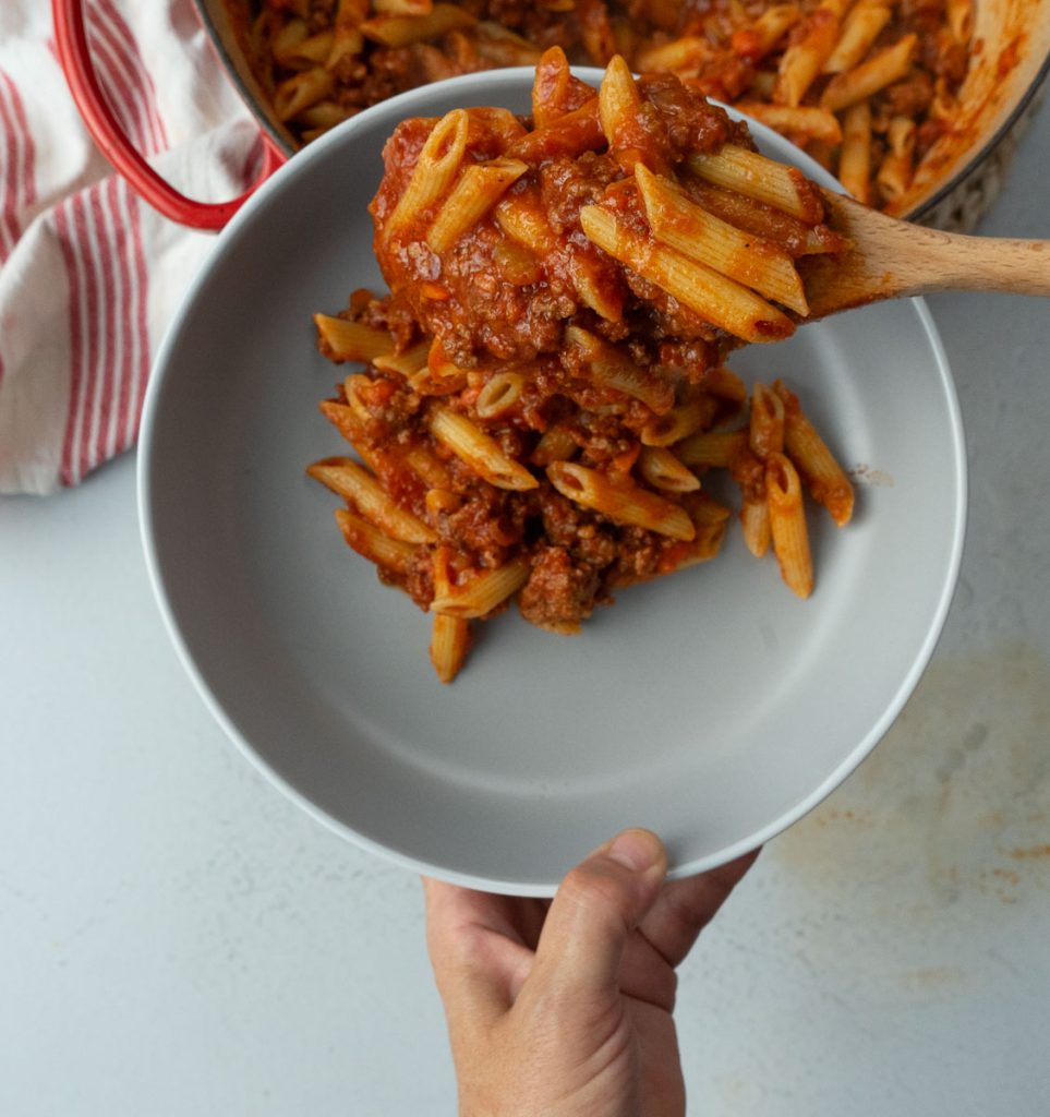 hand holding a gray plate, pasta is being put onto the plate