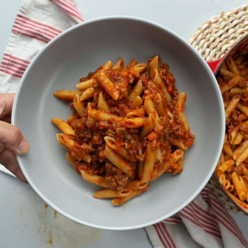 gray plate with pasta and sauce in the middle of it being held up over the table that has a pot of pasta on it