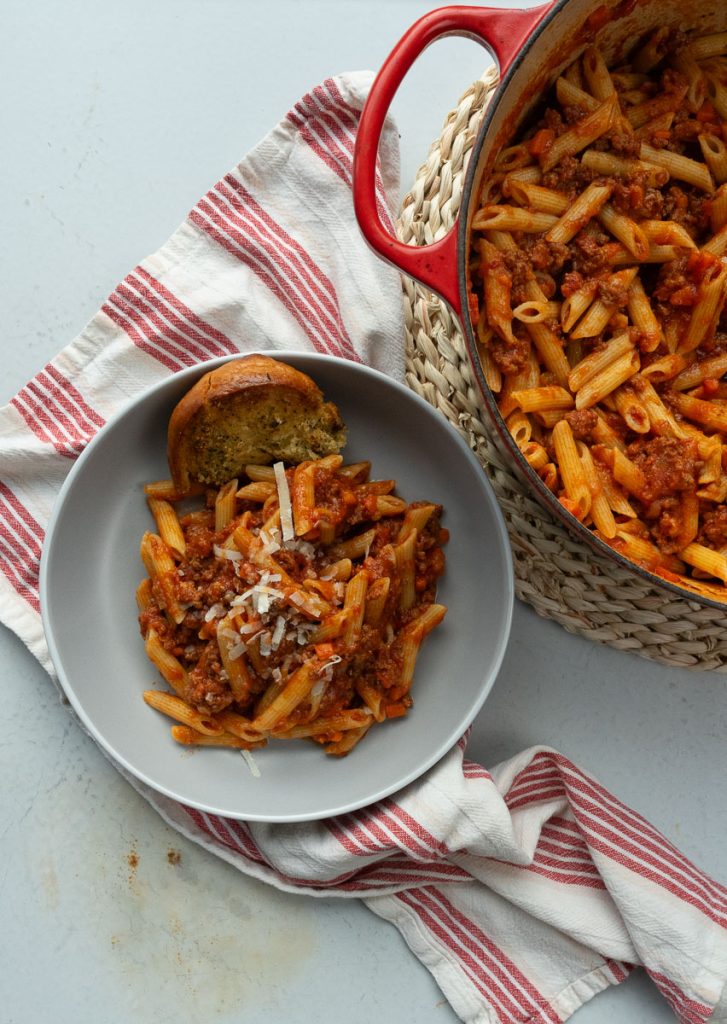 ragu with ziti on a gray plate with garlic bread the red pot of pasta is in the upper right corner