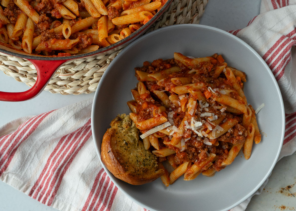 ragu with ziti on a gray plate with garlic bread the red pot of pasta is in the upper left corner