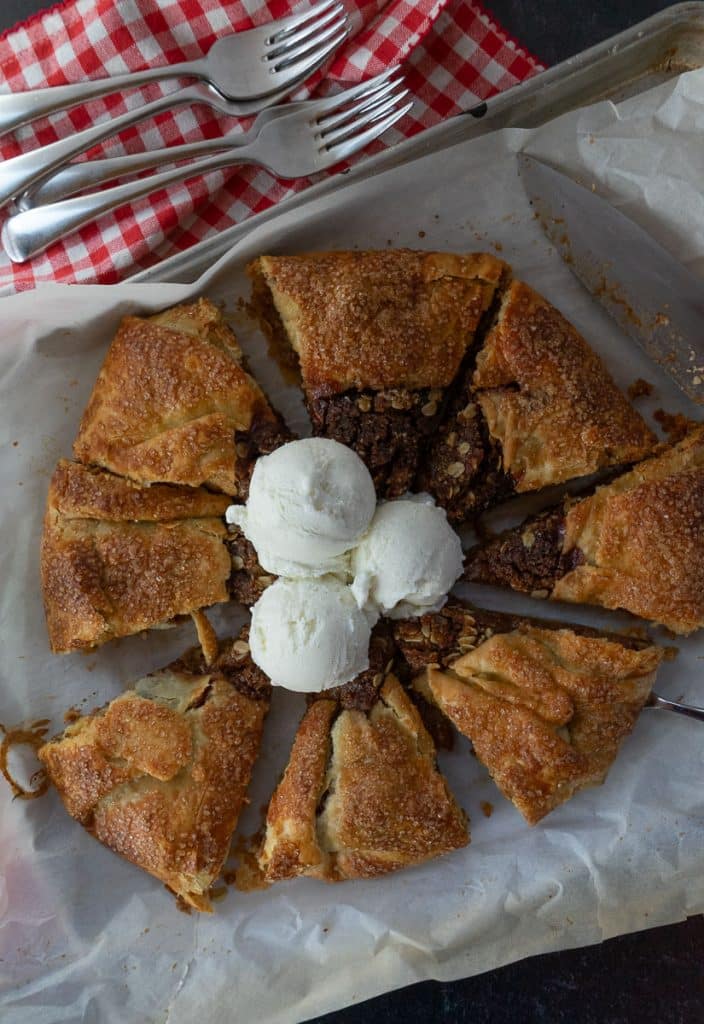 apple crisp galette on the pan with ice cream in the middle red gingham cloth in back ground with forks and the knife is off to the right