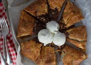 apple crisp galette on the pan with ice cream in the middle red gingham cloth in back ground with forks and the knife is off to the right