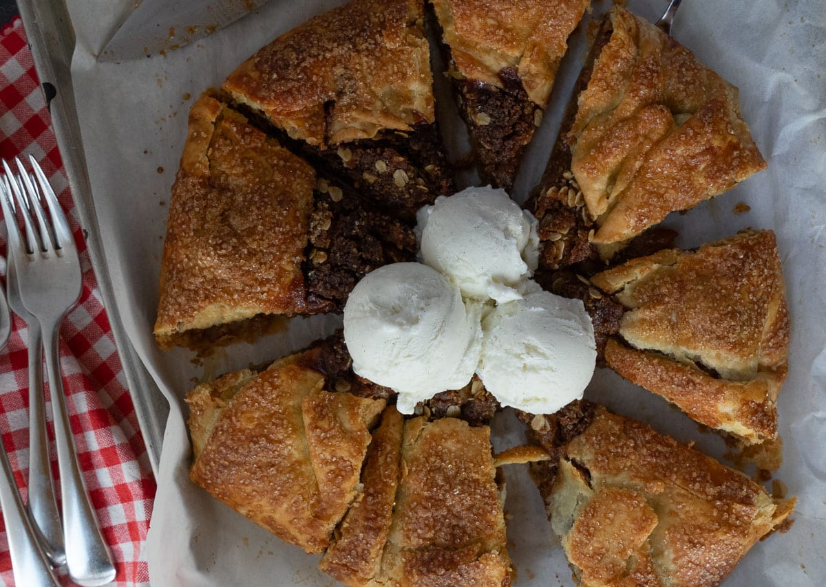 apple crisp galette on the pan with ice cream in the middle red gingham cloth in back ground with forks and the knife is off to the right