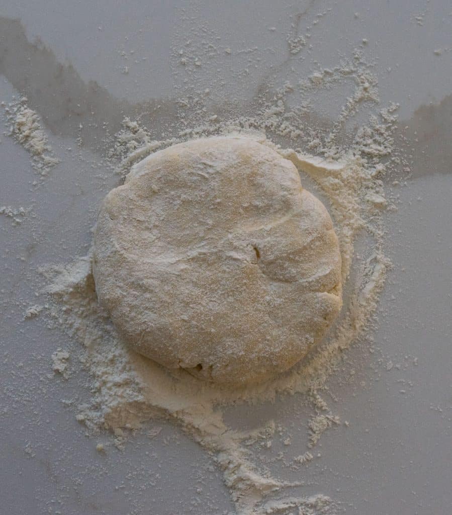 disc of pastry dough on a white countertop with flour dusting around it.
