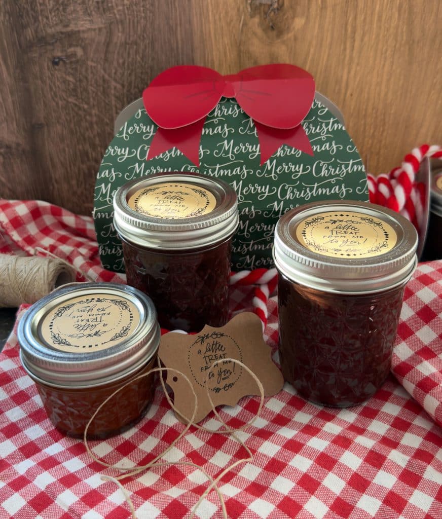 mason jars of hot fudge sauce on a red and white gingham cloth with gift wrappings and ribbons in the background