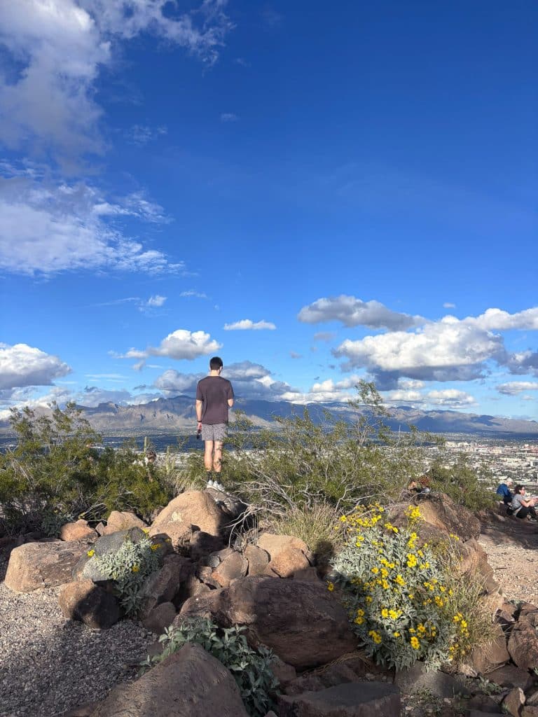 man standing on a large rock over looking the tucson valley below, some fluffy clouds with blue sky
