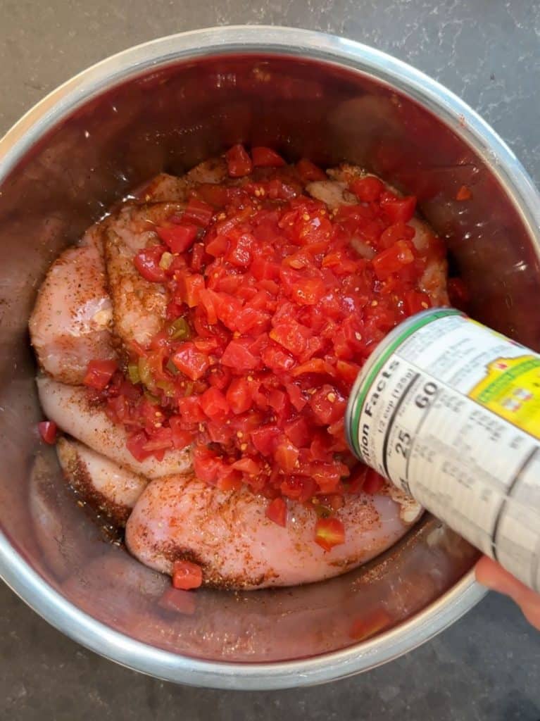 raw chicken breasts in a instant pot with seasonings and pouring a can of diced tomatoes over the chicken