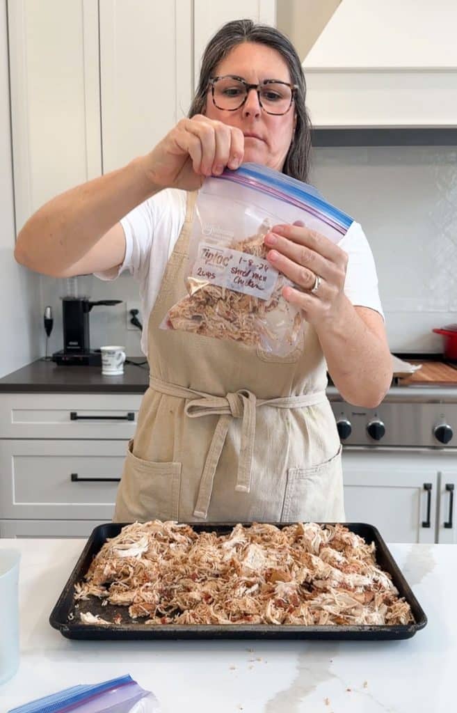 person in a tan apron packaging up shredded chicken in freezer zip-loc bags