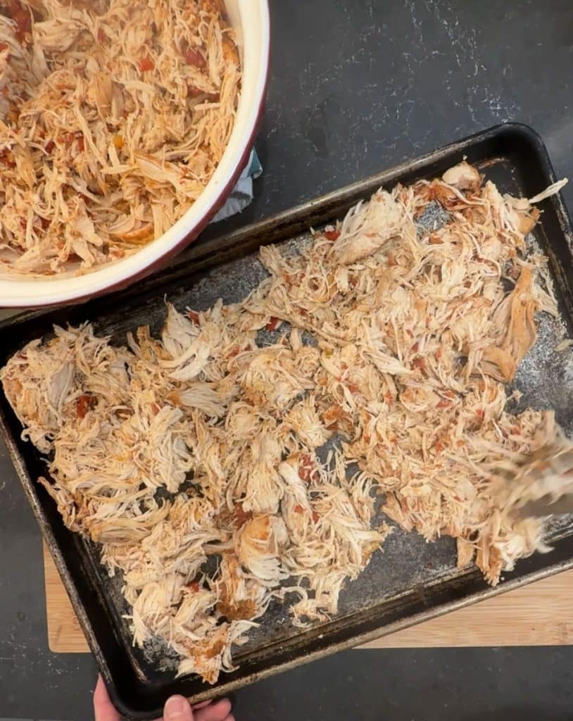 shredded chicken in a bowl, with more shredded chicken on a baking sheet cooling off 