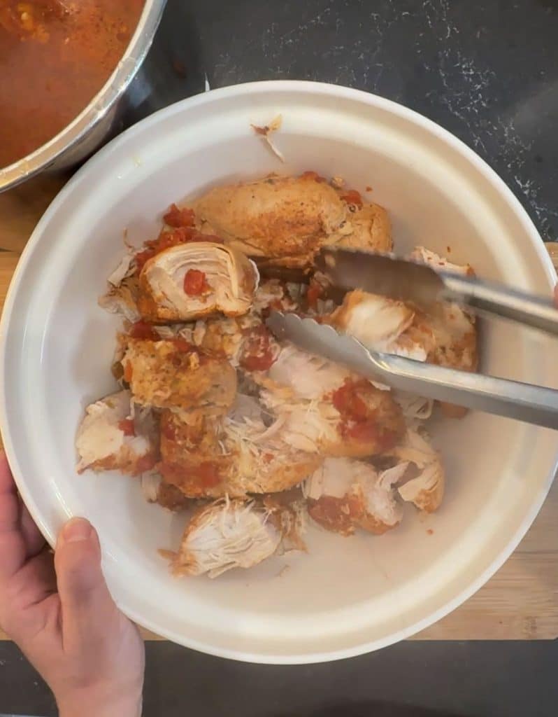cooked chicken in a bowl being pulled apart with tongs