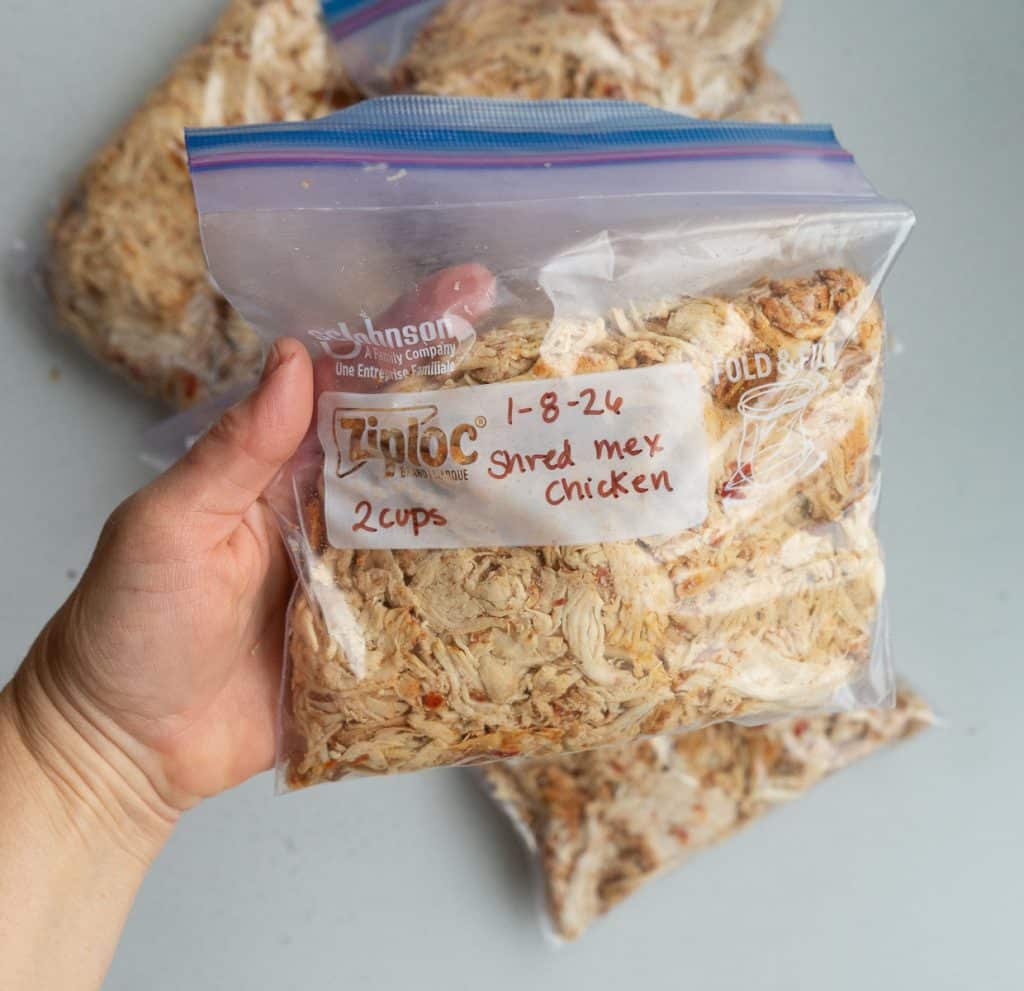 hand holding a freezer bag of shredded chicken over a white countertop