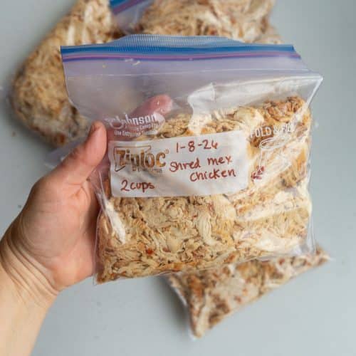 hand holding a freezer bag of shredded chicken over a white countertop
