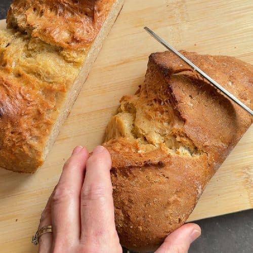 irish soda bread loaf cut in half on a cutting board a hands slicing one half of the loaf