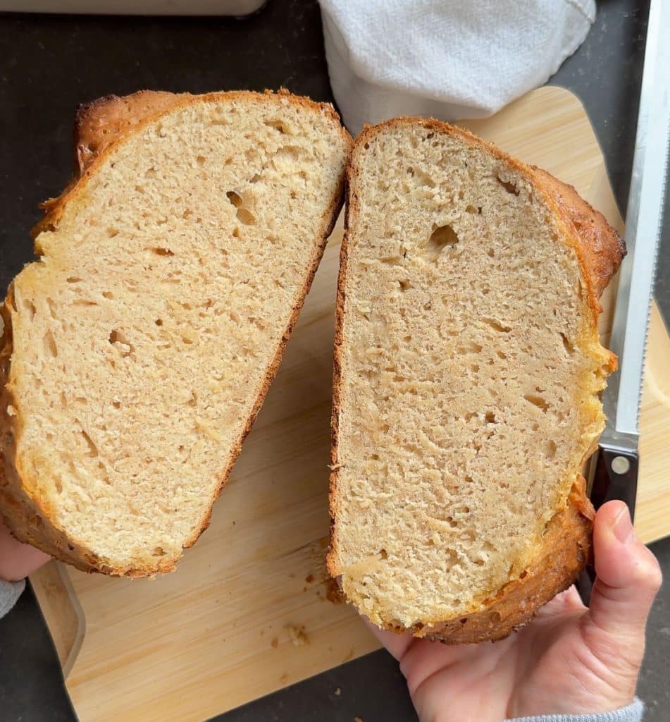 irish soda bread cut in half with hands holding each half over a wood cutting board