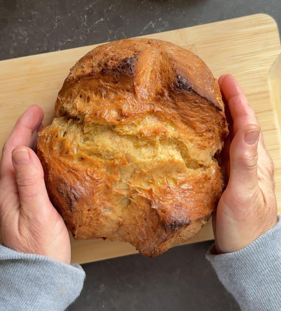 hands setting a loaf of irish soda bread on a wood cutting board